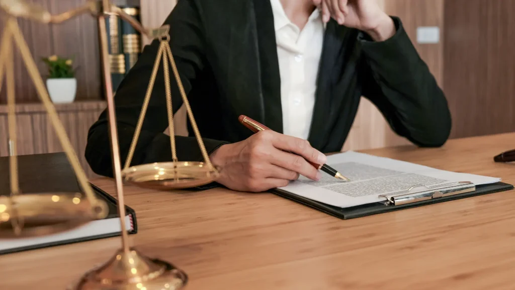 Lawyer writing in a legal document with scales of justice on the table.